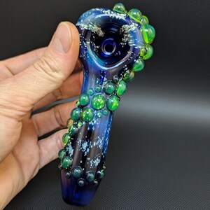 May include: A blue glass pipe with a galaxy design and green glass bubbles around the bowl.