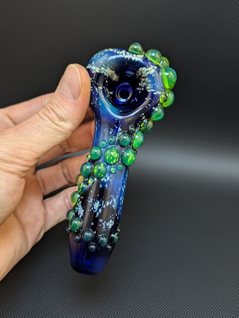 May include: A blue glass pipe with a galaxy design and green glass bubbles around the bowl.