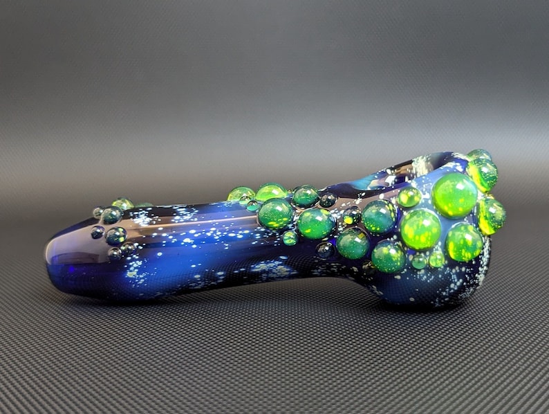 May include: A blue glass pipe with a galaxy-like design and green and yellow glass bubbles.
