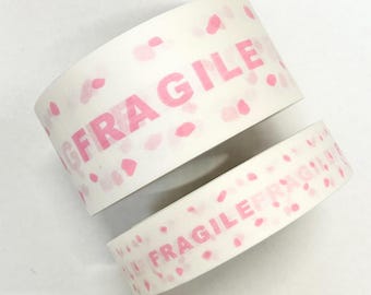 May include: Two rolls of white packing tape with the word "FRAGILE" printed in pink. The tape also features a pattern of pink polka dots. Ideal for shipping delicate items.
