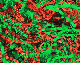 May include: A collection of crinkled paper shreds in vibrant red and green colors. The thin, zigzag-cut paper strips are densely packed together, creating a textured, layered surface of intertwined festive-colored paper strands.