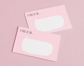 May include: Two pink notecards with a white speech bubble design and the text "A note to say...". The cards are arranged diagonally against a pink background, creating a simple and clean aesthetic.