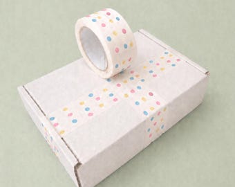 May include: A roll of decorative tape with a polka dot pattern in pink, yellow, and blue sits atop a white cardboard box. The box is sealed with matching polka dot tape, creating a cohesive and colorful presentation.