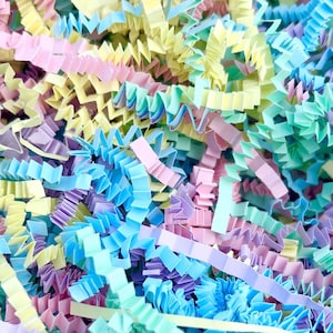 May include: A close-up shot of pastel-coloured crinkle paper, including pink, blue, yellow, and green. The paper is shredded and has a textured, wavy appearance, suitable for gift packaging or decorative use.