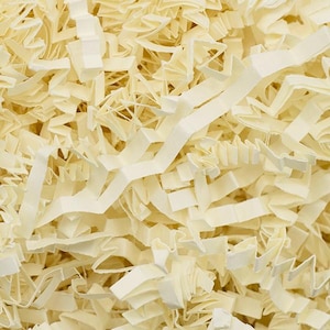 May include: Close-up of cream-coloured paper shred, a packing material. The shredded paper is cut into thin strips and has a textured appearance. The strips are layered and create a full, dense look. The paper is a neutral colour, suitable for various packaging needs.