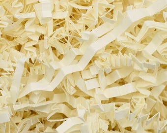 May include: Close-up of cream-colored paper shred, a packing material. The shredded paper is cut into thin strips and has a textured appearance. The strips are layered and create a full, dense look. The paper is a neutral color, suitable for various packaging needs.