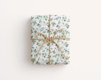 May include: A wrapped gift box featuring a white background with a pattern of green leaves and stems. The box is tied with natural twine, forming a bow. The overall aesthetic is clean and natural.