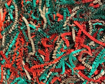 May include: A dense collection of crinkled paper shreds in vibrant red, teal, and natural tan colors. The thin, zigzag-cut paper strips are intertwined to create a textured, multi-colored filler material for gift packaging and displays.