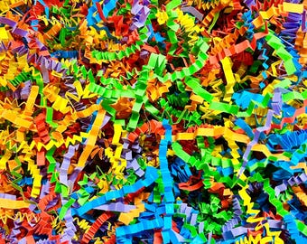 May include: A close-up view of colorful shredded paper. The paper is a mix of red, orange, yellow, green, blue, and purple. The paper is cut into thin strips and has a crinkled texture. This decorative paper is often used for gift packaging.