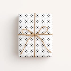 May include: A wrapped gift with white polka dot paper and tied with twine. The twine is tied in a bow around the package. The gift is rectangular and sits on a white surface.