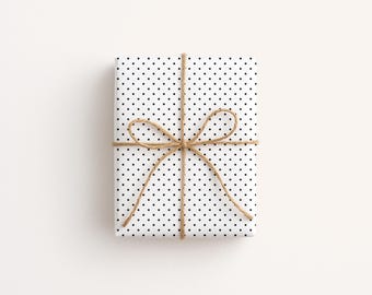 May include: A wrapped gift with white polka dot paper and tied with twine. The twine is tied in a bow around the package. The gift is rectangular and sits on a white surface.