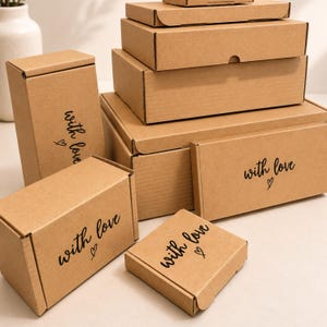 May include: A collection of brown cardboard shipping boxes in various rectangular and square sizes. Each box features the black printed text "with love" accompanied by a small hand-drawn heart symbol on the front or top surface.