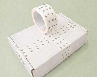 May include: A roll of decorative tape with a pattern of small green dots sits atop a white cardboard box. The tape is used to seal the box, with additional tape strips applied. The background is a solid light green.