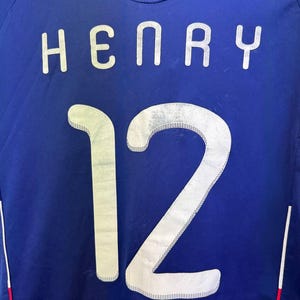 May include: A blue soccer jersey with the name "HENRY" and the number "12" in white, outlined with a silver trim. The jersey has the text "Federation Fran&ccedil;aise de Football" at the top.