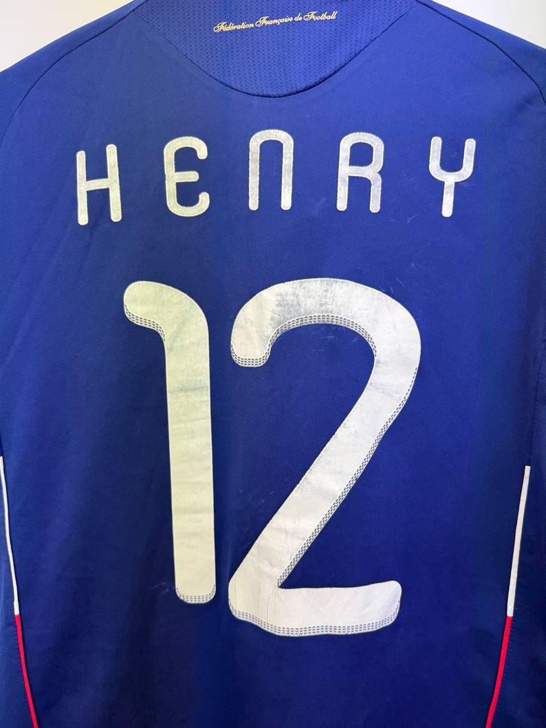May include: A blue soccer jersey with the name "HENRY" and the number "12" in white, outlined with a silver trim. The jersey has the text "Federation Fran&ccedil;aise de Football" at the top.