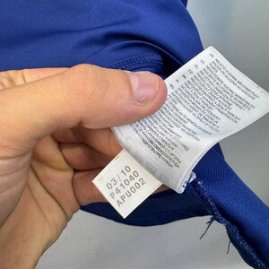 May include: Close-up of a blue athletic shirt with a white tag. The tag displays the numbers "03/10", "P41040", and "APU002". The shirt's fabric is visible, along with the stitching.