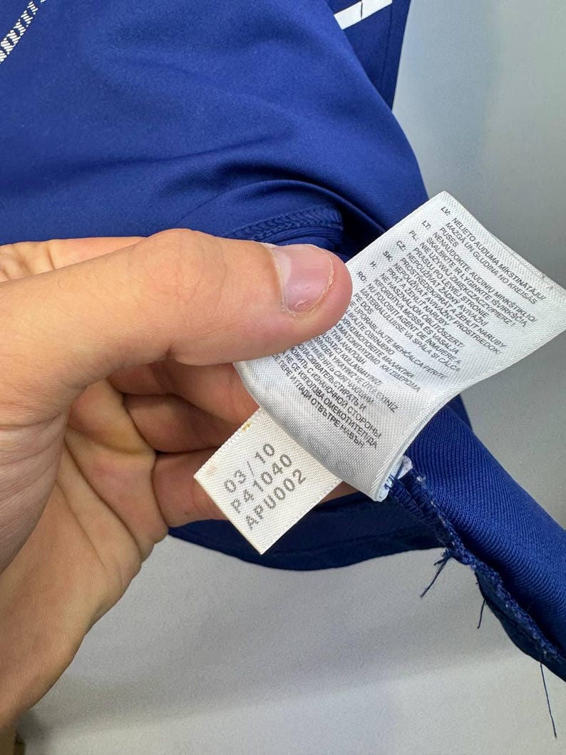 May include: Close-up of a blue athletic shirt with a white tag. The tag displays the numbers "03/10", "P41040", and "APU002". The shirt's fabric is visible, along with the stitching.