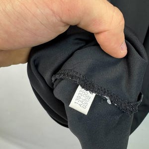 May include: Black garment with a tag attached. The tag has the numbers "139333", "AAL00", and "03/02" printed on it. The garment is made of a smooth, dark fabric.