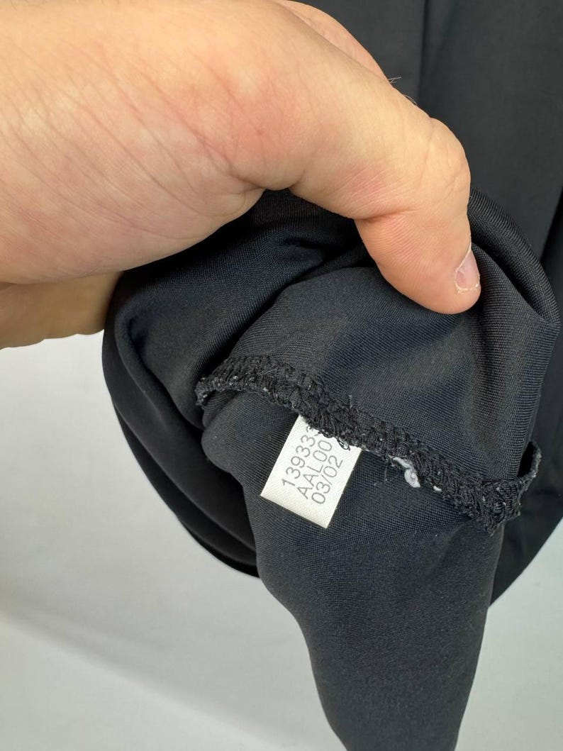May include: Black garment with a tag attached. The tag has the numbers "139333", "AAL00", and "03/02" printed on it. The garment is made of a smooth, dark fabric.