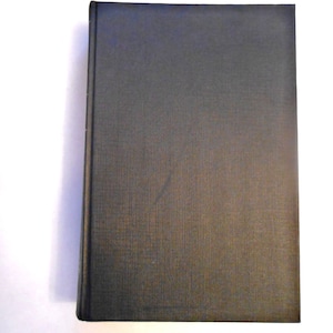 May include: A hardcover book with a dark gray cover. The cover has a textured appearance and a spine on the left side. The book is set against a white background.
