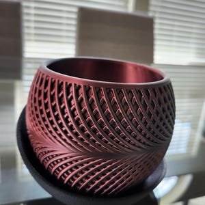 Puede incluir: Una maceta roja con un patrón geométrico. La maceta está hecha de un material texturizado y tiene una forma redonda.