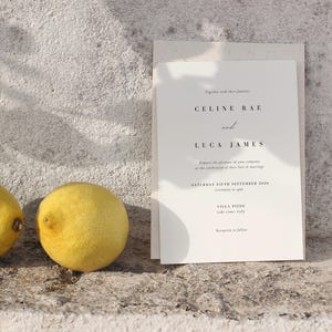May include: A wedding invitation with the names Celine Rae and Luca James printed in elegant black font. The invitation includes the date, time, and location of the ceremony at Villa Pizzo, Lake Como, Italy. Two yellow lemons are in the foreground.