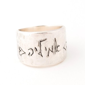 May include: A silver ring with a textured surface and Hebrew writing engraved on the band.
