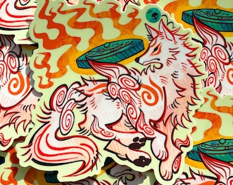 May include: A die-cut sticker featuring a stylized white wolf with orange swirling markings, surrounded by orange flames and a teal circular disc. The wolf is depicted in a dynamic pose against a pale yellow background with a small teal circular logo.