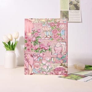 May include: A rectangular notebook cover featuring a collage of pink roses, tulips, and illustrations of clothing and accessories. The design includes a teacup filled with roses, a glass of pink liquid, and script text on a light pink background.