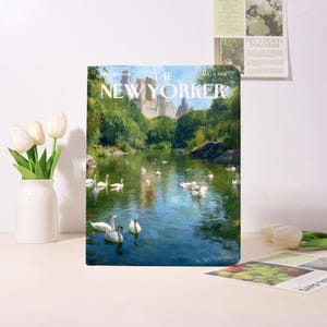 Può includere: Una copia della rivista The New Yorker del 4 agosto 1965, con un dipinto di un lago con cigni e alberi. La rivista è esposta con un vaso di tulipani bianchi e altri oggetti decorativi.