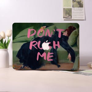 May include: Laptop skin featuring a painting of a woman in a black dress reclining on a green sofa. The words "DON'T RUSH ME" are in pink over the image, with the Apple logo incorporated. The overall theme is art and relaxation.