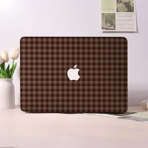 Könnte beinhalten: Ein Laptop mit einem dunkelbraunen und hellbraunen Vichy-Karomuster auf dem äußeren Deckel. In der Mitte des Deckels befindet sich ein weißes Apple-Logo. Das Design bedeckt die gesamte Oberfläche des Laptop-Deckels in einem gleichmäßigen Raster.