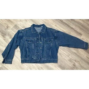 May include: A medium-wash denim jacket with a button-up front, two chest pockets, and two side pockets. The jacket has a classic collar and long sleeves. The denim is a solid blue color.