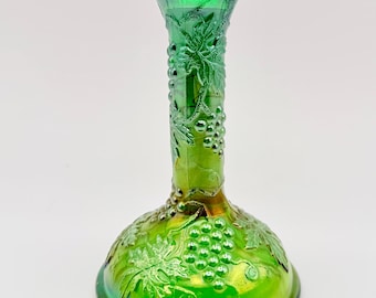 May include: A vibrant green iridescent glass candlestick holder featuring a raised relief pattern of grape clusters and vine leaves wrapping around the cylindrical stem and the wide, circular base of the piece.