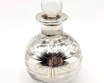May include: A clear glass perfume bottle with a spherical body and a round stopper. The bottle features horizontal silver stripes and a prominent silver floral design on the front. The neck of the bottle has a silver-colored rim finish.