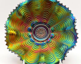 May include: A round iridescent carnival glass bowl featuring a scalloped edge and a central medallion with a floral pattern. The surface displays a vibrant spectrum of metallic green, blue, and gold hues with repeating concentric petal-like ridges.