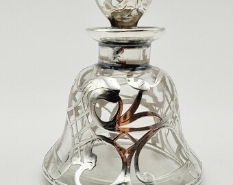 May include: A clear glass bell-shaped perfume bottle featuring an intricate silver-colored metal overlay with swirling floral patterns. The bottle includes a matching spherical glass stopper with silver metal accents at the top and neck.