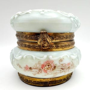 May include: A vintage, light blue trinket box with a floral design and gold-colored metal accents. The box features a hinged lid and a decorative clasp. The base of the box has hand-painted pink flowers and leaves.
