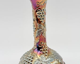 May include: A candlestick holder featuring an iridescent finish with shifting hues of purple, gold, and blue. The surface is decorated with raised, silver-toned relief patterns of grape clusters and vine leaves wrapping around the cylindrical stem.