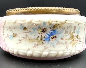 May include: A decorative, antique glass bowl with a brass rim. The bowl features hand-painted blue and white floral designs on a cream-colored background, with a pink rim and a textured, rope-like border.