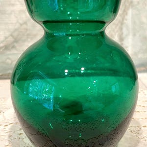 May include: A vibrant green glass vase with a rounded body and a flared rim. The vase has a glossy finish and a darker, textured pattern near the base. This decorative vase is suitable for displaying flowers or as a standalone accent piece.
