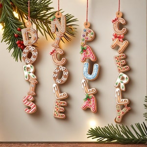 May include: Gingerbread cookie ornaments spelling out "DORIS NICOLE PAULA CHERYL" with red string and wooden tags. Each letter is decorated with icing and festive details, perfect for holiday decor.
