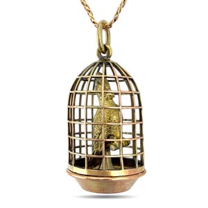 May include: A gold-toned pendant necklace featuring a bird in a cage design. The cage is detailed with vertical and horizontal bars, and the bird is perched inside. The necklace has a delicate chain.