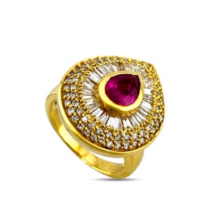 May include: A gold ring featuring a central pear-shaped ruby surrounded by a halo of baguette-cut white stones and an outer border of small round white stones. The setting is crafted in a yellow gold tone with a polished finish throughout.