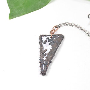 May include: A silver chain necklace with a triangular pendant made of copper and white enamel. The pendant has a textured, organic design.