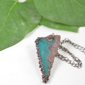 May include: A teal green and copper pendant necklace with a textured, irregular shape. The pendant is attached to a silver chain.