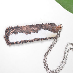 May include: A silver chain necklace with a rectangular pendant. The pendant is made of copper and has a white, textured surface. The pendant has a small, round, copper accent.