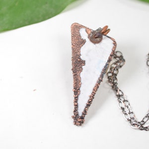 May include: A white and copper triangle pendant necklace with a silver chain. The pendant has a rough, textured surface and a small metal accent.