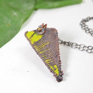 May include: A triangular pendant necklace with a textured copper finish and a bright yellow enamel design. The pendant is attached to a silver chain.