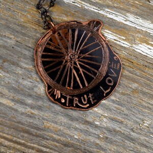 May include: A copper necklace featuring a wheel-shaped pendant with the words "TRUE LOVE" inscribed around the edge.